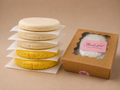Three uncooked Classic and two uncooked Chocolo arepas beside The Daily Arepa box.